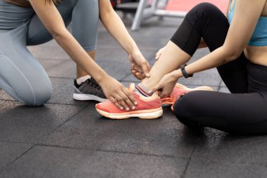 Spor salonunda egzersiz yaptıktan sonra ayak bileği ağrıyan Asyalı genç bir kadın. Egzersiz eğitiminde acı veriyor ve arkadaşlar yardım etmek ve teşvik etmek için buradalar.