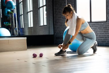 Ayakkabı bağlayan genç Asyalı kadın spor salonunda, penceresi doğal ışık olan bir odada egzersiz yapmaya hazır ol. Fitness ve sağlıklı yaşam tarzı konsepti geliştirmeye başlıyor.
