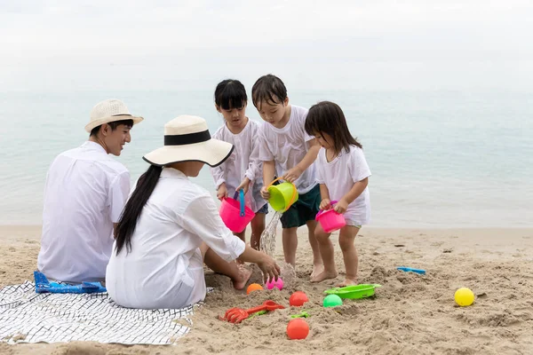 Happy Asian Family Five people On Summer Vacation playing toys on sand in the beach together In the morning time, sunrise. Holiday and Travel concept.