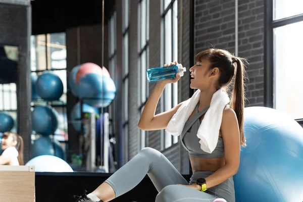 Young woman asian drink water after workout In a room with a window with natural light. Fitness and healthy lifestyle concept