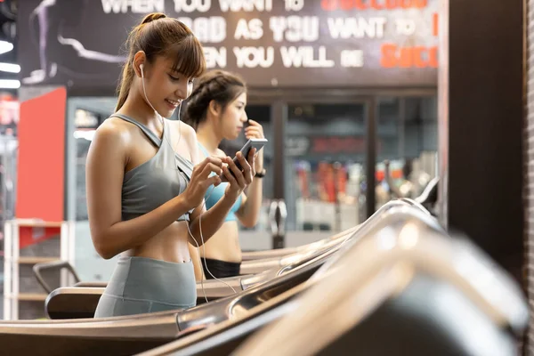 Asian woman running on track and listening to music with smart phone in hand using earphones. Fitness, healthy and lifestyle concept