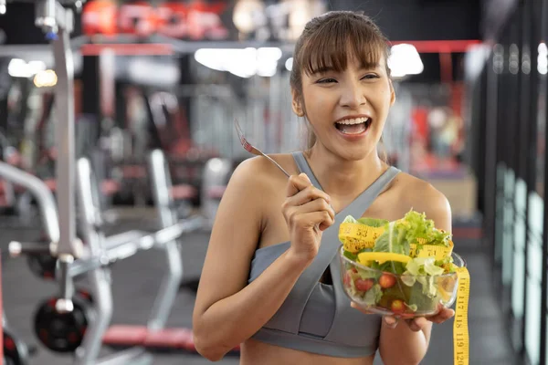 Healthy asian young woman Happy eating vegetables green salad at gym. Fitness and healthy food , lose weight concept