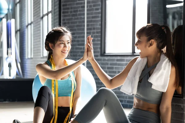Healthy asian two people young woman making high five gesture in gym after workout In a room with a window with natural light. Smiling successful fitness class after training