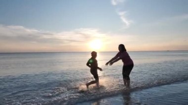 Mutlu Asyalı Aile Yaz Tatili Oğlu annesinin yanına koşuyor ve akşam günbatımında kumsalda sarılıp birlikte dönüyorlar. Tatil, mutlu aile zamanı ve seyahat konsepti. Yavaş çekim