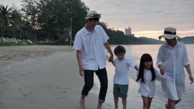 Mutlu Asyalı Aile Dört kişi yaz tatilinde. Baba, anne, oğul ve kız. Kumsalda el ele yürüyorlar. Tatil ve Seyahat kavramı. 