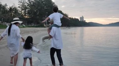 Arka manzara Mutlu Asyalı Aile Yaz Tatili 'nde dört kişi el ele yürüyor ve Oğul sabah gün doğumunda sahilde boyuna biniyor. Tatil ve seyahat konsepti. Yavaş çekim