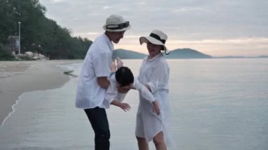 Mutlu Asyalı Aile Yaz Tatili Kızı sabah vakti kumsalda anne ve babalarıyla birlikte uçuyor. Gün doğumunda. Tatil ve seyahat konsepti. Yavaş çekim