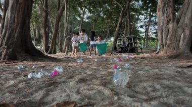 Asyalı aile babası, anne, oğul ve kız çöpleri toplamak için birbirlerine yardım ederler plajda plastik şişeleri yeşil plastik torbaya koyarlar. Güvenli ekoloji ve geri dönüşüm kavramı. Yavaş Hareket