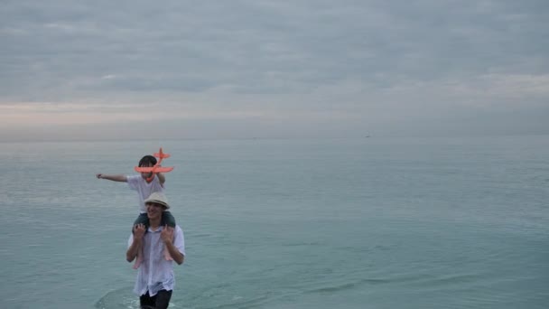 Happy Asian Family On Summer Vacation Son on fathers shoulders playing plane flying together Walking on the beach In the morning time, sunrise. Holiday and Travel concept. Slow motion