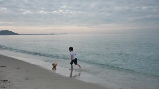 快乐的亚洲孩子们在沙滩上踢足球夏天的假期早上 假日和旅行的概念 慢动作 — 图库视频影像
