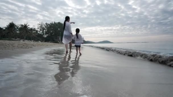 夏休みに幸せなアジアの家族母と娘が一緒にビーチで手を携えて歩く朝の時間には 日の出 休日と旅行の概念 スローモーション — ストック動画