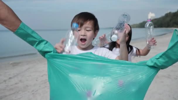 亚洲家庭父亲 儿子和女儿互相帮助 在海滩上把垃圾 塑料瓶收集成绿色塑料袋 安全生态和回收概念 慢动作 — 图库视频影像