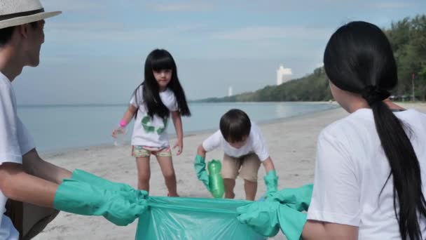 アジアの家族父 娘ゴミ プラスチックボトルをビーチの緑のビニール袋に集めるのに役立ちます 安全な生態系とリサイクルの概念 スローモーション — ストック動画