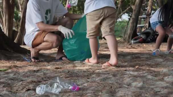 アジアの家族父 娘ゴミ プラスチックボトルをビーチの緑のビニール袋に集めるのに役立ちます 安全な生態系とリサイクルの概念 スローモーション — ストック動画