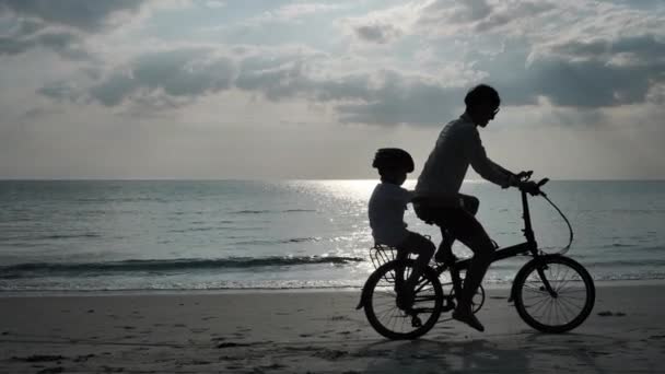 亚洲家庭暑假爸爸和儿子骑自行车在海滩度假和旅行的概念 轮廓慢动作 — 图库视频影像