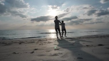 Mutlu Asyalı genç çift el ele tutuşup kumsalda sarılıyorlar. Denizde günbatımı. Tatil ve seyahat konsepti. Yavaş Hareket