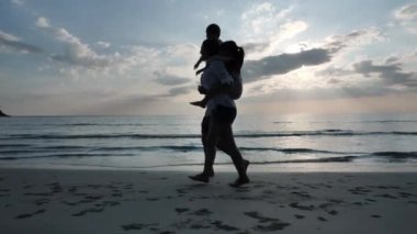 Mutlu Asyalı Aile Yaz Tatili Oğlu, Kızı sırt sırta Babalar ve annesi sahilde birlikte yürüyor. Denizde günbatımı. Tatil ve seyahat konsepti. Yavaş çekim