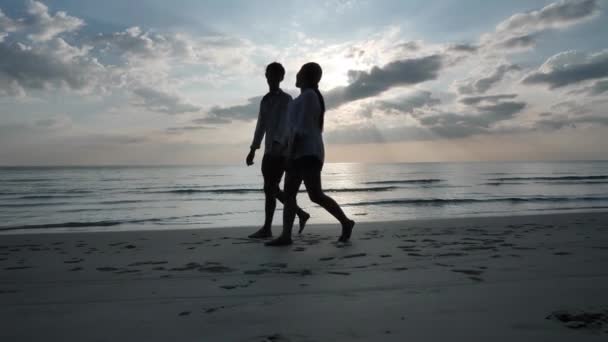 サイドビューハッピーアジアの若いカップルは 手をつないで歩いてビーチで一緒に遊ぶのが大好きです 海の背景日没 休日や旅行のコンセプト スローモーション — ストック動画