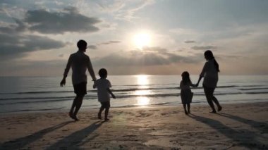 Mutlu Asyalı Aile Yaz Tatili Baba, anne, oğul ve kız el ele tutuşup birlikte sahile doğru koşuyorlar. Denizde günbatımı. Gevşe Tatil ve Seyahat konsepti. Yavaş çekim