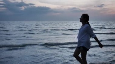 Mutlu Asyalı kadın akşamları sahilde yürürken rahatlıyor, Sunset. Tatil ve seyahat konsepti. Yavaş çekim 