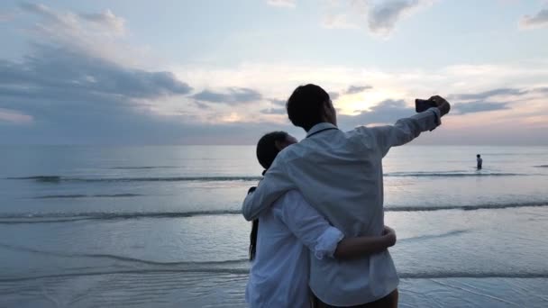 사랑하는 아시아인젊은 부부는 스마트폰으로 자신의 사진을 해변의 백지해 곳에서 하늘을 — 비디오