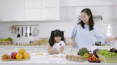 Mutlu Asyalı aile anne bak. Küçük kız kahvaltısını yapıyor. Evde sütlü mısır gevreği yiyor. Sağlıklı gıda konsepti Vücudun gücü için