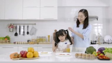 Mutlu Asyalı aile anne ve küçük kız kahvaltı yapıyorlar, mısır gevreği ve süt ve portakal suyu evde. Sağlıklı gıda konsepti Vücudun gücü için