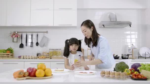 幸せなアジアの家族お母さんと女の子は自宅でキッチンで朝食 牛乳とオレンジジュースでシリアルを食べています 健康食品の概念体の強さのために — ストック動画