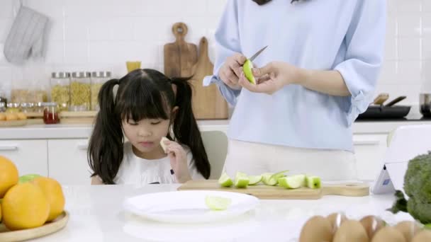 快乐的亚洲家庭妈妈们正在厨房里准备蔬菜和水果 女儿在厨房里玩智能手机 健康食品和晨间活动概念 — 图库视频影像