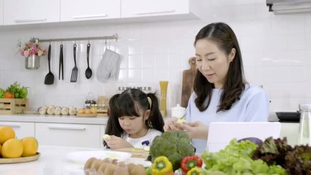 快乐的亚洲家庭妈妈们正在厨房里准备蔬菜和水果 女儿在厨房里玩智能手机 健康食品和晨间活动概念 — 图库视频影像