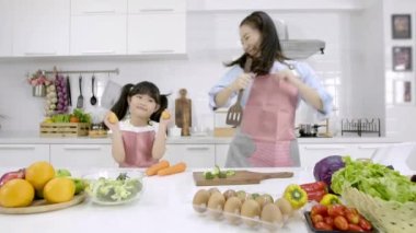 Mutlu Asyalı bir aile, neşeli bir anne ve küçük bir kız evdeki mutfak odasında en sevdiği şarkıyla dans ediyorlar. Aktif eğlence ve yaşam tarzı konsepti. Yavaş çekim