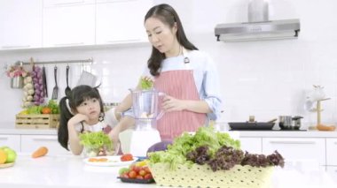 Mutfaktaki mutlu Asyalı aile. Anne ve küçük kız salatayı evde blender menüsünde lezzetli bir meyve suyu ve malzemeyle hazırlıyorlar. Yemek pişirme, sağlıklı gıda konsepti