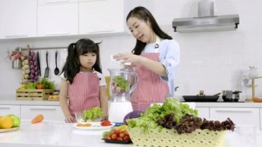 Mutfaktaki mutlu Asyalı aile. Anne ve küçük kız salatayı evde blender menüsünde lezzetli bir meyve suyu ve malzemeyle hazırlıyorlar. Yemek pişirme, sağlıklı gıda konsepti