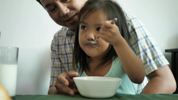 子供たちの近くの女の子は自宅で父と一緒に座ってミルクと朝食のシリアルを食べる スローモーション — ストック動画
