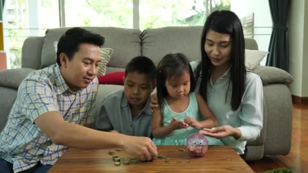 亚洲家庭在家里母亲 父亲和两个孩子 女儿一起在家里的客厅里用储蓄罐存钱 储蓄家庭概念 — 图库视频影像