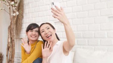 Mutlu Asyalı aile anne ve genç kız akıllı telefonla evde güneş ışığı olan bir odada video konuşuyorlar. İletişim teknolojisi konsepti. Yavaş Hareket