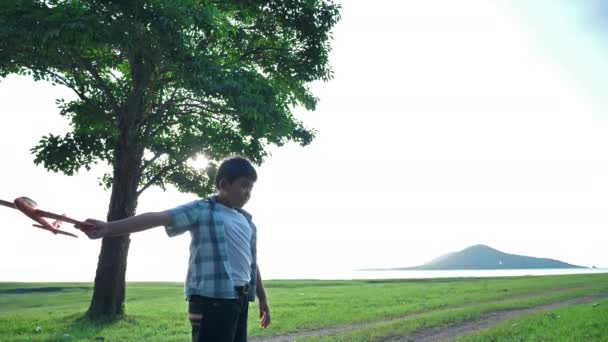 Šťastné asijské dítě chlapec házejí hrát letadlo simulovat v přírodě, stromy a travnaté porosty venku, který má sluneční světlo ve večerních hodinách. Šťastná dovolená Pomalý pohyb
