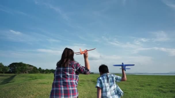 幸せなアジアの母親と息子彼らは夕方に太陽の光がある自然 草原で一緒に飛行機のシミュレーションを実行しています 家族の幸せの休日スローモーション — ストック動画