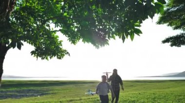 Mutlu Asyalı anne ve oğul, doğada, ağaçlarda ve otlaklarda birlikte uçak simülasyonu yapıyorlar. Akşamları güneş ışığı alan yerlerde. Aile Mutluluğu Tatili Yavaş Hareket