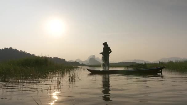 湖のボートで日没時に漁網を投げる漁師のシルエット コンセプトフィッシャーマンズライフスタイル タイのロッブリ — ストック動画