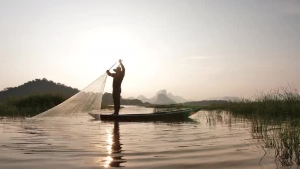 漁網を放り投げた後 漁師は漁網を引きます湖でボートと日没時に コンセプトフィッシャーマンズライフスタイル タイのロッブリ スローモーション — ストック動画
