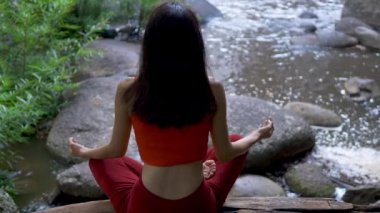 Arkadan bakan Asyalı kadın şelalede yoga yapıyor, Lotus meditasyon seansında poz veriyor. Güzel manzara, doğal arka plan, Tayland.