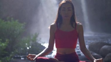 Şelalede yoga yapan ya da pratik yapan Asyalı kadını kapatın, meditasyon seansında Lotus pozu verin. Güzel manzara, doğal arka plan, Tayland.