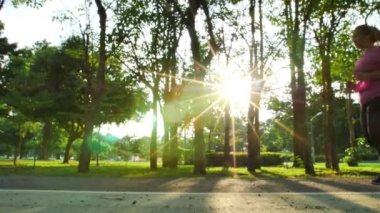 Yavaş hareket eden Asyalı kadınların koşuşunu, parkta ve akşam güneşinde koşuşunu. İyi sağlık ve egzersiz.