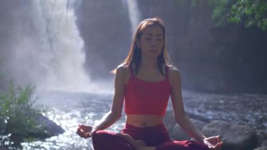 Şelalede yoga yapan ya da pratik yapan Asyalı kadını kapatın, meditasyon seansında Lotus pozu verin. Güzel manzara, doğal arka plan, Tayland.