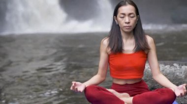 Şelalede yoga yapan ya da pratik yapan Asyalı kadını kapatın, meditasyon seansında Lotus pozu verin. Güzel manzara, doğal arka plan, Tayland.