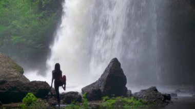 Şelalede yoga yapan Asyalı bir kadın. Güzel manzara, doğal arka plan, Tayland. Kadın profesyonel yoga.