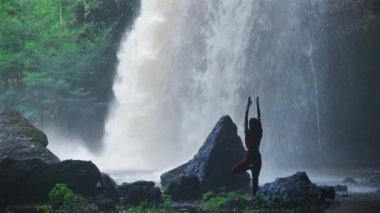 Şelalede yoga yapan Asyalı bir kadın. Güzel manzara, doğal arka plan, Tayland. Kadın profesyonel yoga.