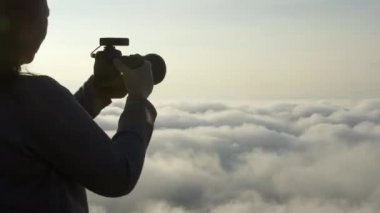 Kadın fotoğrafçının arka görüntüsü, sabah DSR kamerasıyla fotoğraf çekiyor ve güneş doğarken dağın zirvesinde sis, deniz sisi arka planında. Turizm, Seyahat, Profesyonel Fotoğrafçı