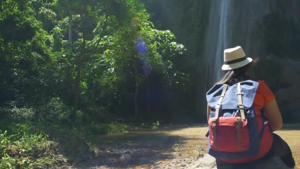 森の中でバックパッカーアジアの女性のバックビューとリラックスし 滝を見て座って楽しむ 森林旅行の冒険でハイキングするハイカー Asia Thailand — ストック動画
